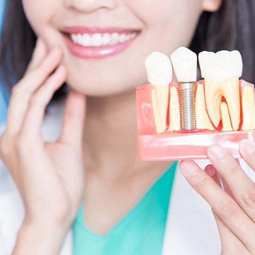 Dentist holding sample implant in one hand and touching her jaw with the other